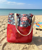 Red Suncheeter Sandshaker beach bag with patterned trim, standing on sand at the beach