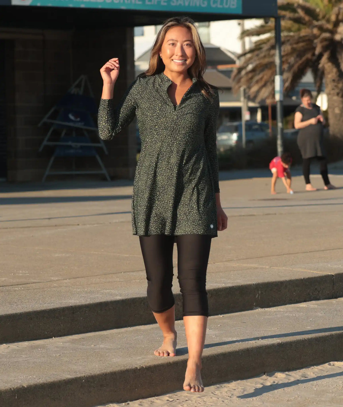 Woman wearing a green spot print long sleeve swim dress with black swim leggings, UPF50+ full coverage swimwear