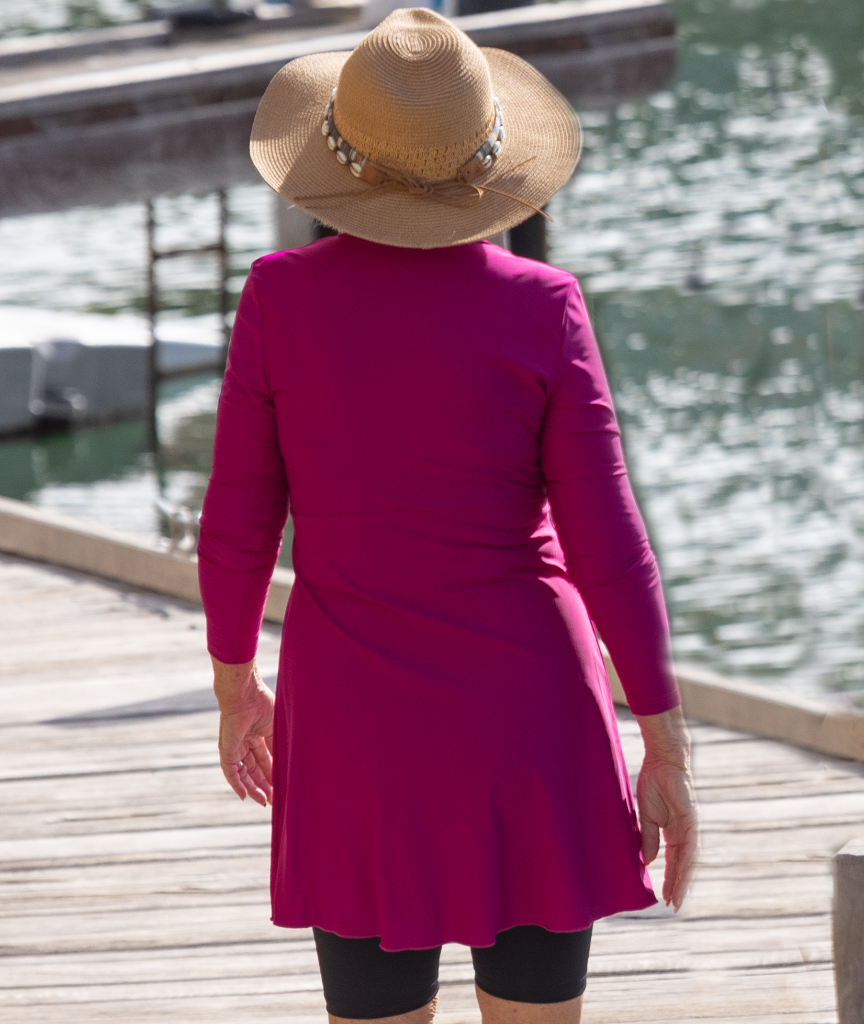 Older woman wearing a pink swim dress and straw hat by a waterfront