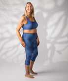 woman in blue print crop top and swim leggings standing against a wall
